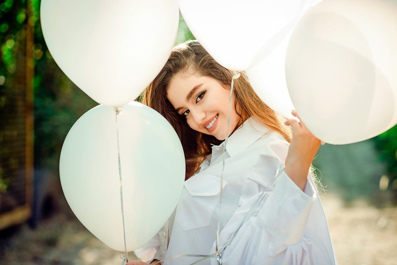 Customer peeks through bunch of white balloons while grinning.