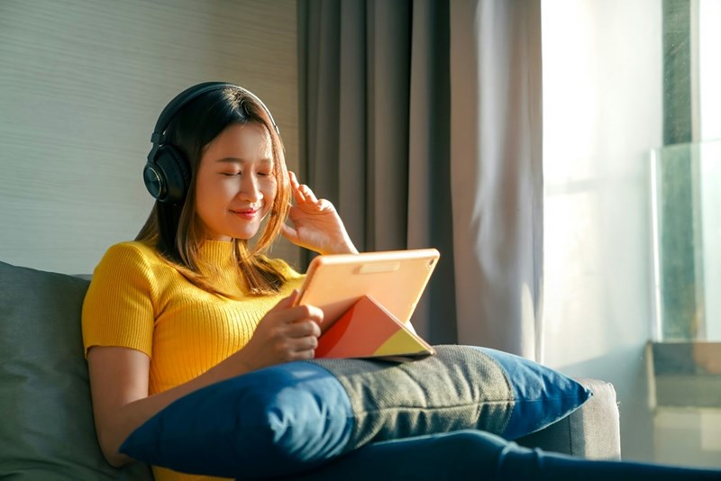 Teen girl relaxes on the couch, happily listening to music in her headphones.