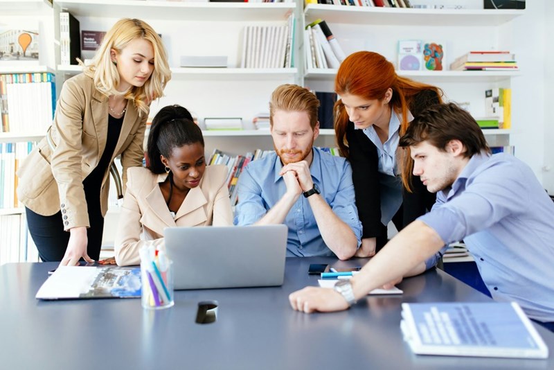 Group of 5 coworkers gather around 1 laptop to solve a problem together.