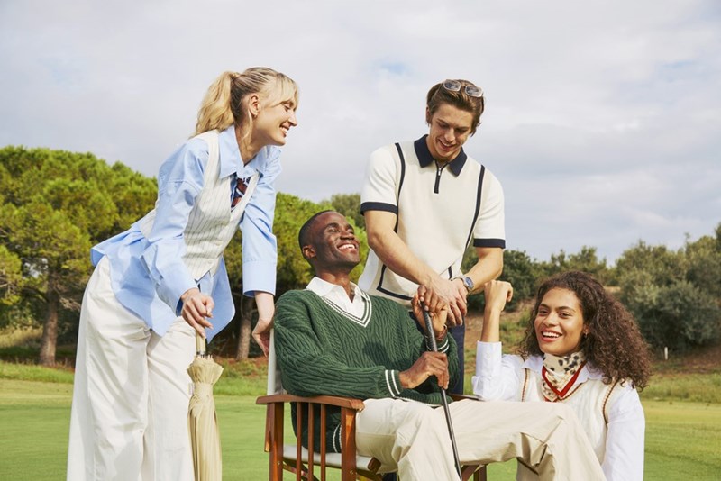 A group of preppy golfer standing a man sitting on a chair on the green