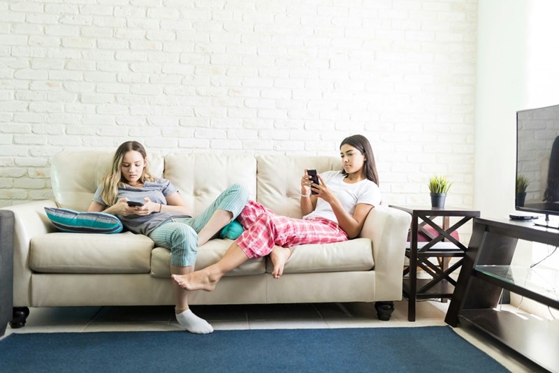 Teenage cousins playing on their smartphones on the couch at a sleepover in the basement