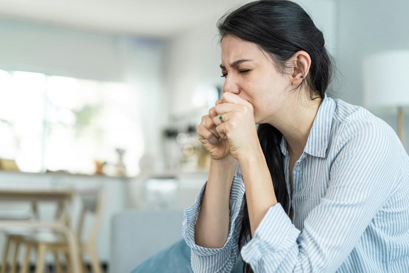 A woman sits upset on the edge of her couch