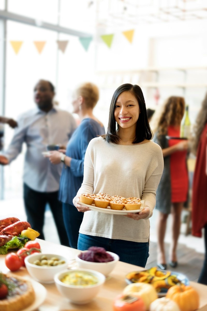 A woman carrying a plate of cupcakes to a potluck buffet table