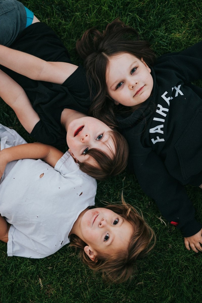 Three young children lie down on grass together