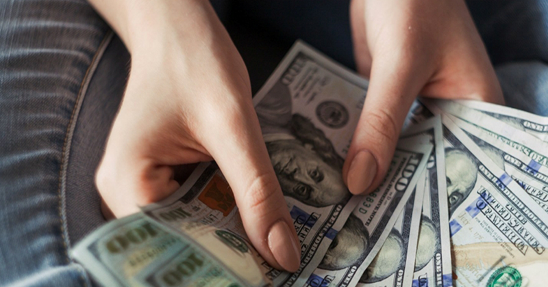 A woman's hands hold a fan of 100 dollar bills
