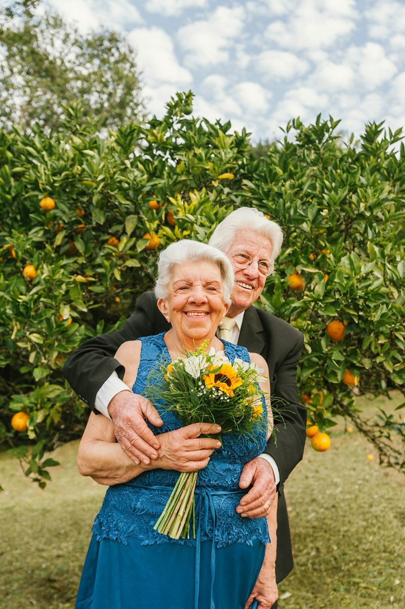 An older couple embracing each other in front of an orange tree