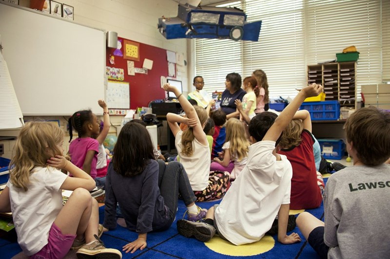 A classroom full of kids sitting on a blue carpet