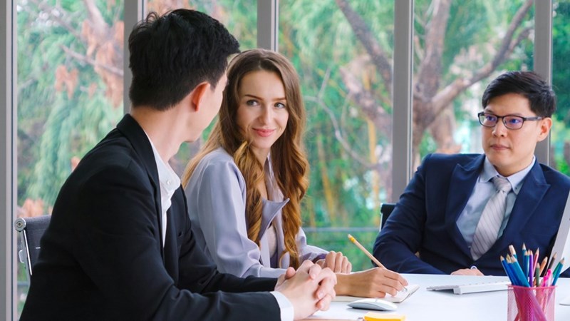 2 interviewers look at candidate, while one woman writes down answers, in a conference room setting.