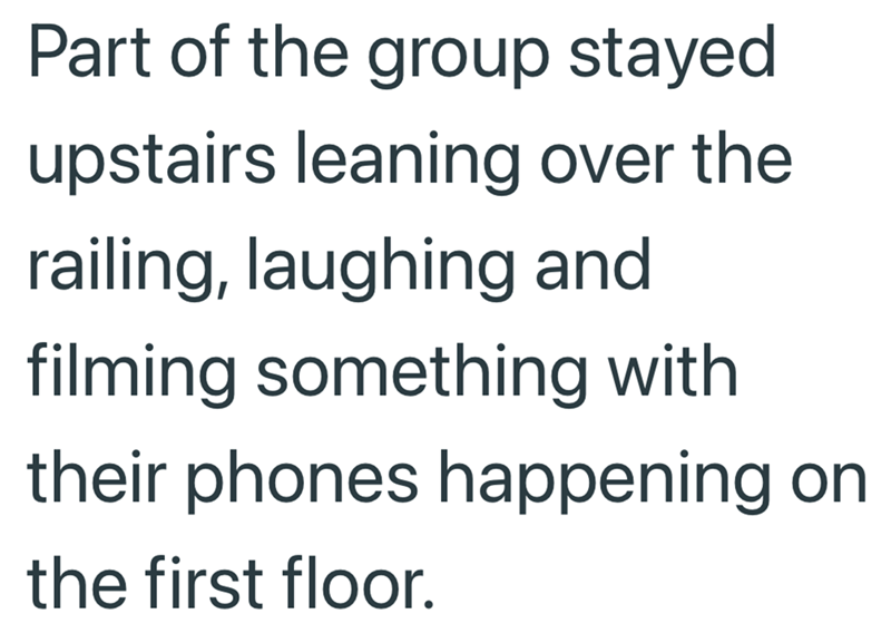 Part of the group stayed upstairs leaning over the railing, laughing and filming something with their phones happening on the first floor.