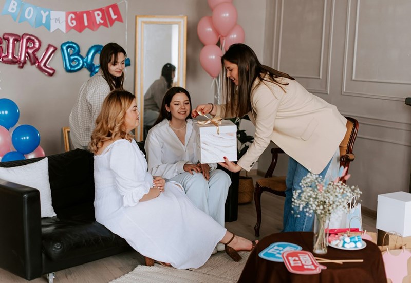 A group of women celebrate a baby shower as one guest presents the mom-to-be with a gift.