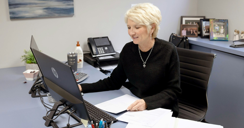 An older female employee sits at a desk and works on a computer