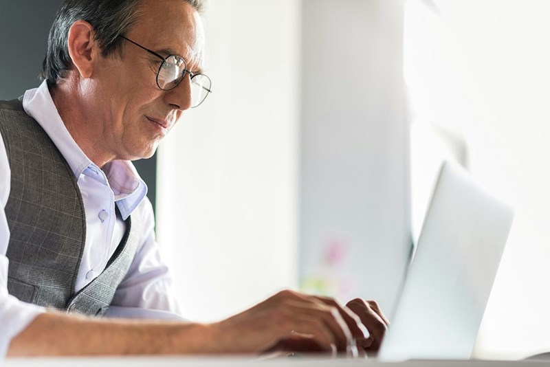 Serious mature man typing on laptop intently while working in office