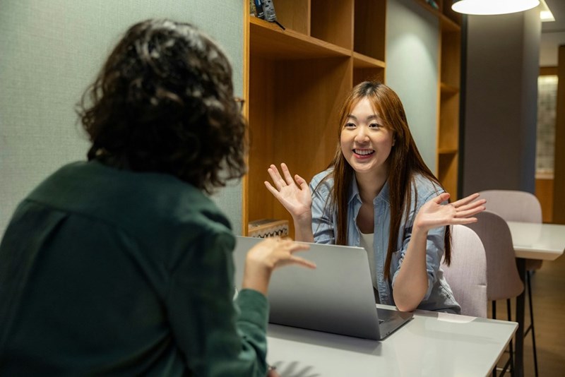 An employee smiles as she tries to charm her manager, sitting opposite her.