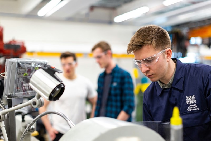 Man in blue and white checked shirt wearing safety glasses while working in engineering