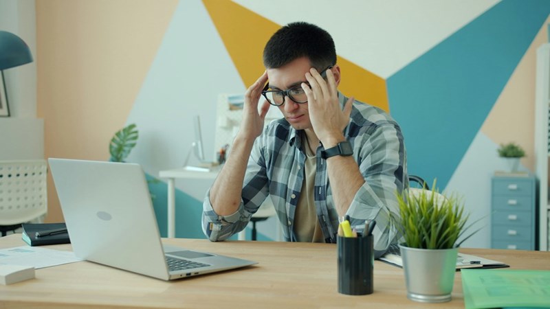 Man holding head in frustration at desk with laptop