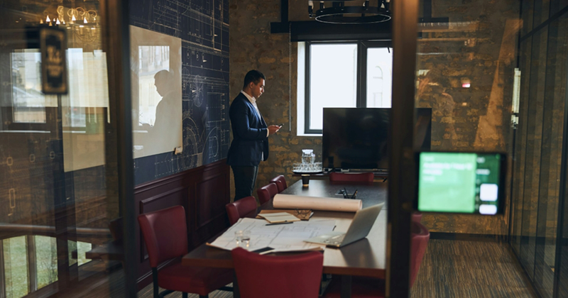 A businessman stands in an empty meeting room, using his phone
