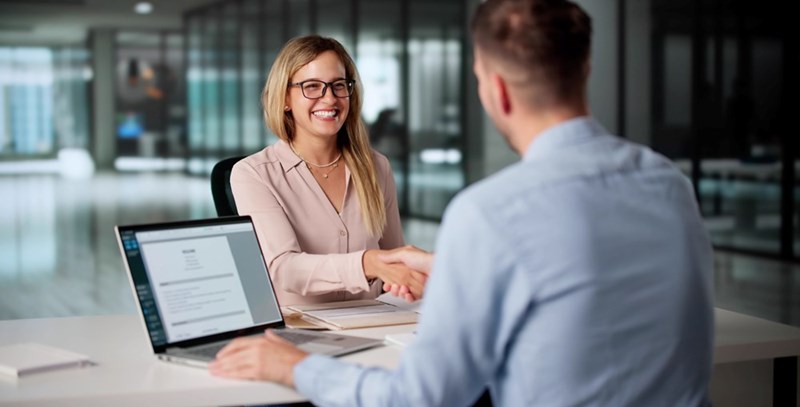 Smiling woman shaking hands with a man across a desk during a successful job interview in a modern office.