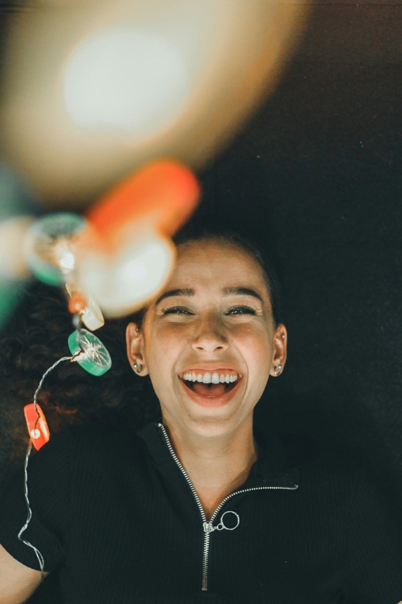 A young woman laughs next to a string of fairy lights