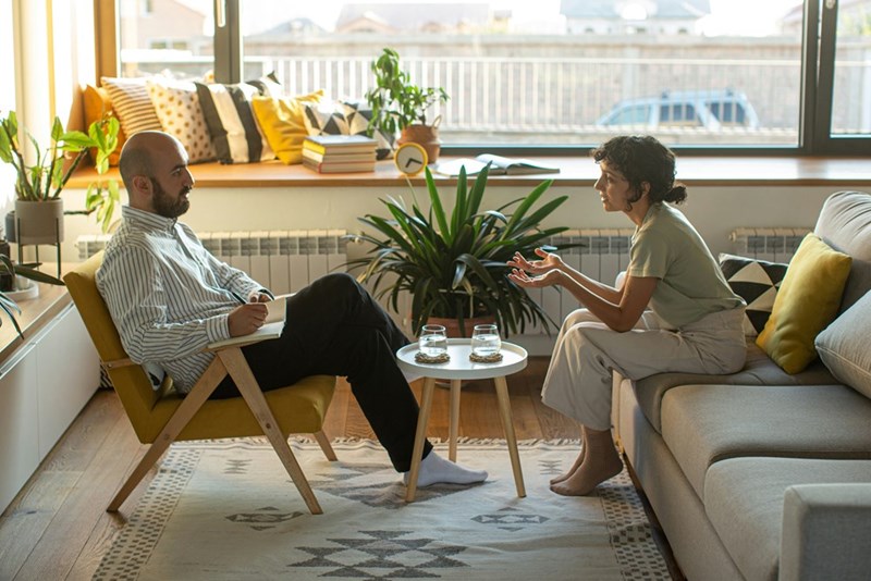 A woman sitting on a couch and talking to her male therapist