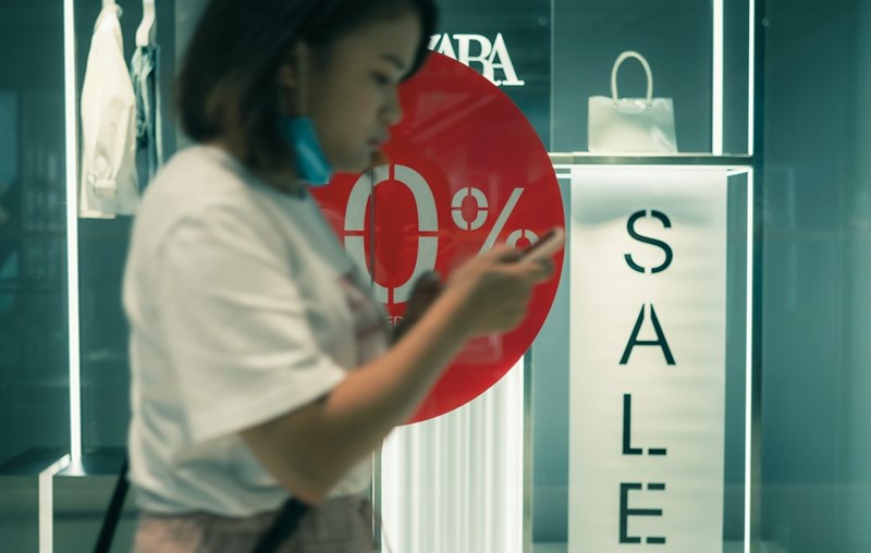 A retail worker in a white t shirt stands in front of a store at a mall