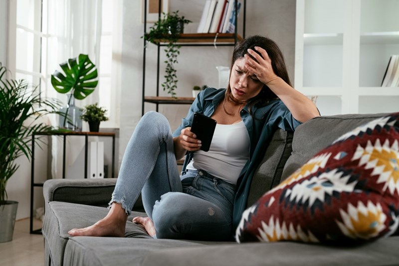 A woman looks at her phone upset on the edge of her couch