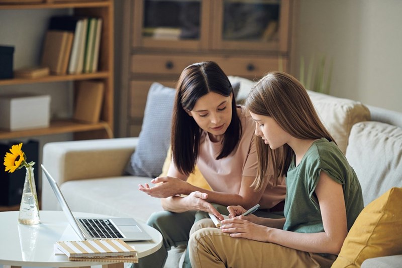 A teenage daughter and her mother have an argument on a couch, looking at a note