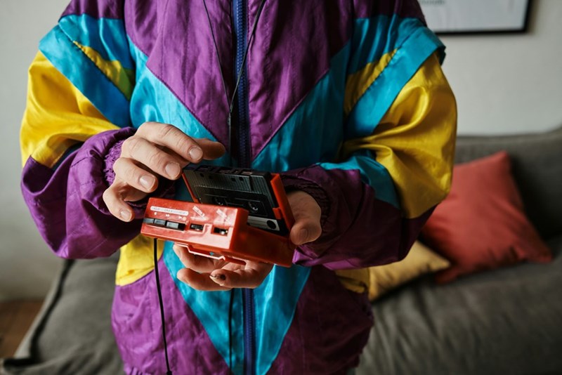 Employee wears 80s themed colorful jacket to office party, while holding tape cassette player from the same time period.