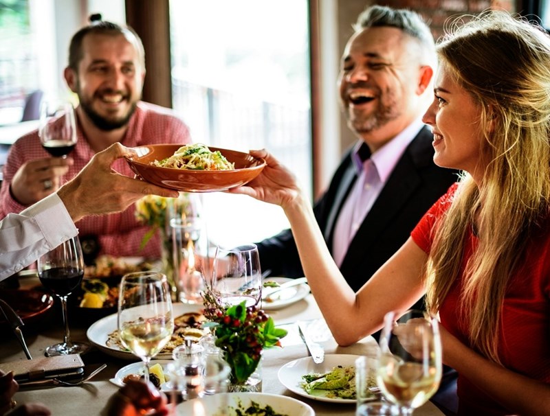 Diners laugh together as a waiter hands a woman a plate of salad.