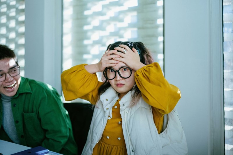 Worker holds head after getting fired while her coworker looks at her and laughs.