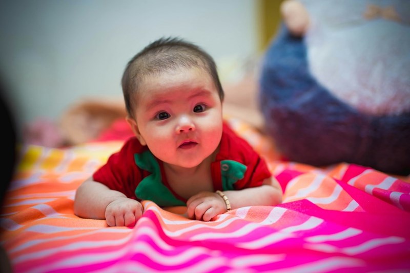 Baby in green shirt lying on her stomach on pink and white striped bed