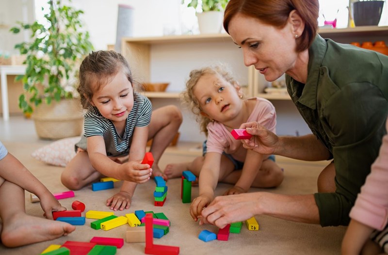 A group of small nursery school children with female teacher on floor in classroom playing
