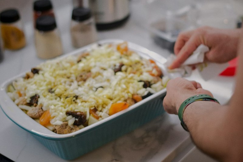 A casserole in a ceramic dish with someone cutting into it and serving themself some food