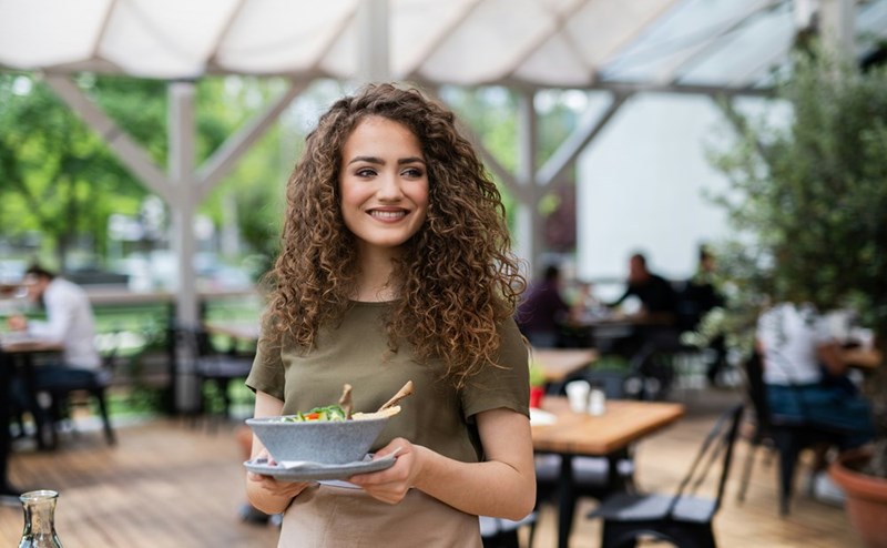 A waitress holds a plate walking across a restaurant terrace