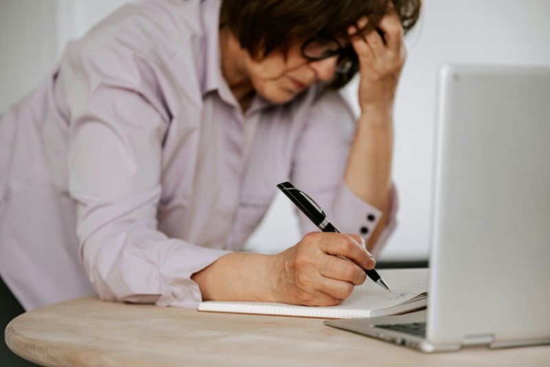 A woman looks stressed while writing and using a laptop