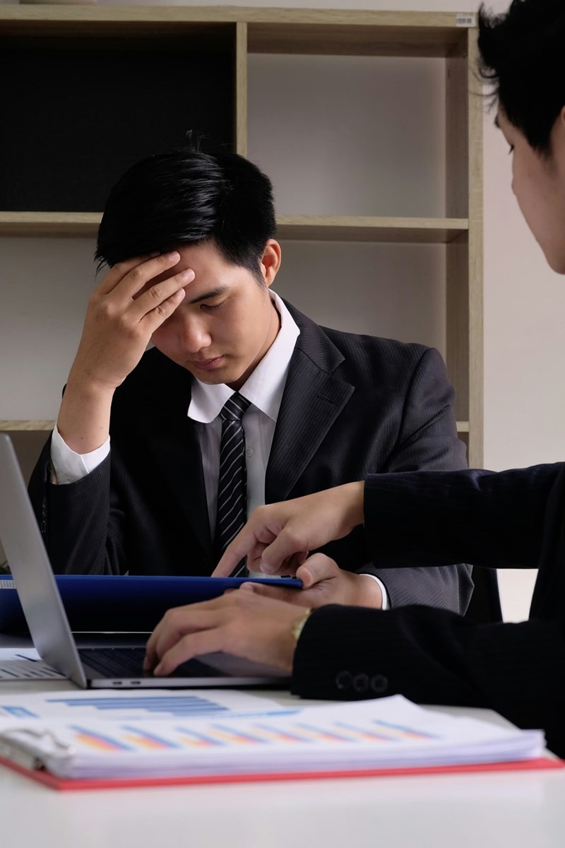 Boss points out employee's mistake, while employee holds his head in embarrassment.