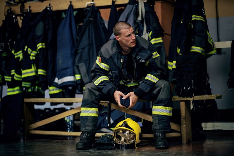 Young attractive fireman in protective uniform sitting in fire station and waiting for other firemen as he prepares for action