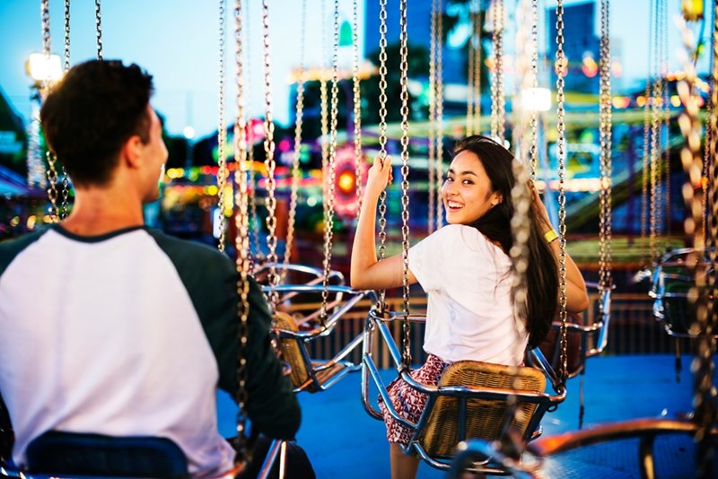 Woman holds onto swing ride while looking back and smiling at a friend.