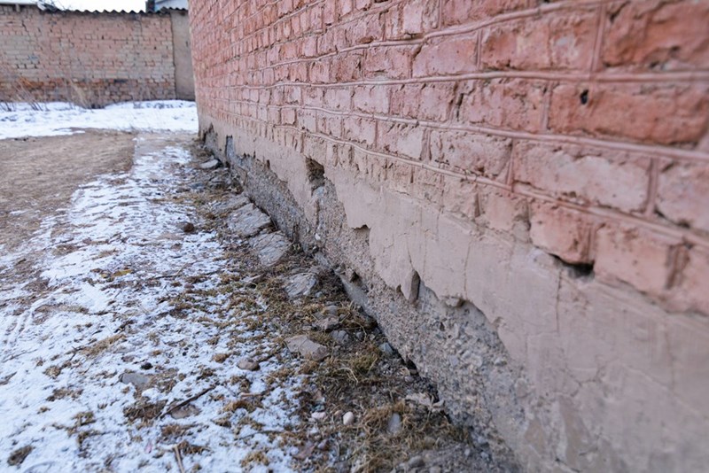 The side of a brick house is affected by excess water runoff.