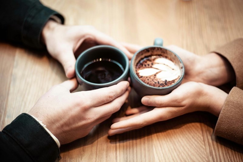 Two people hold mugs together on a date