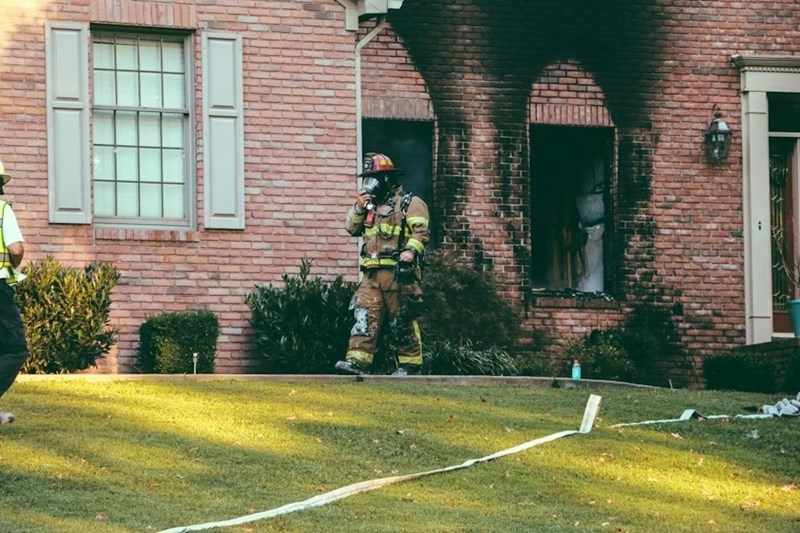 A fireman walking in front of a burned brick house.