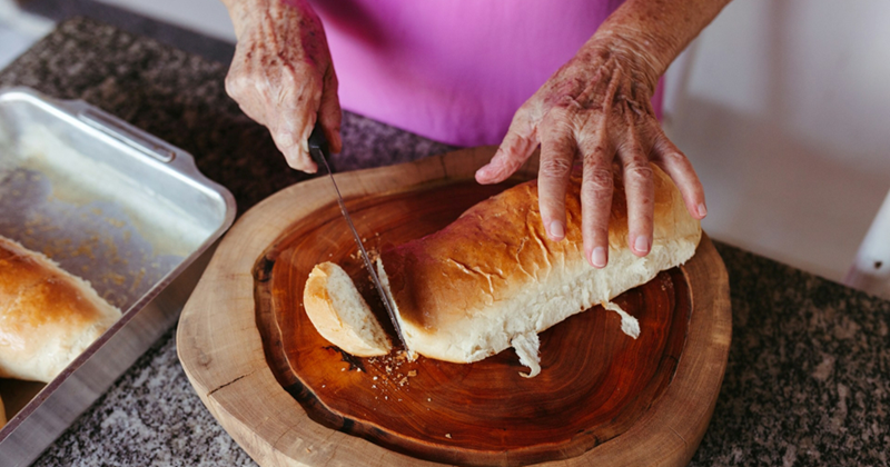 The hands of an older woman cutting bread on a chopping board