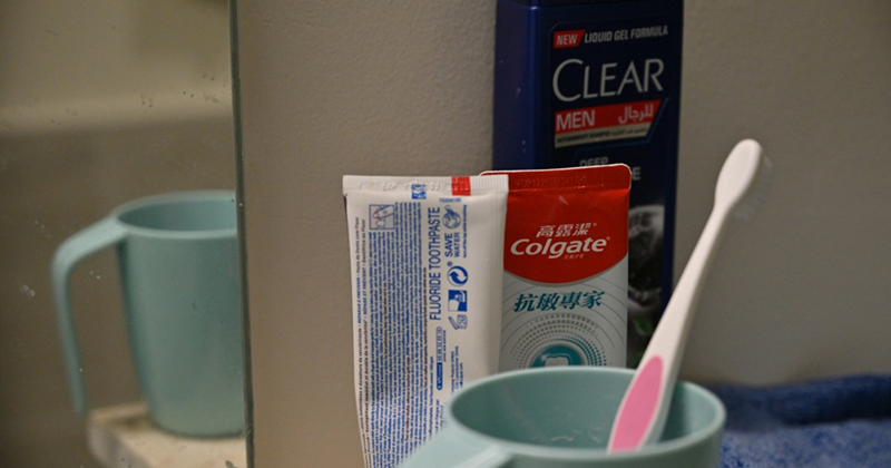 Toothbrush in a mug, toothpaste, and a bottle of soap next to a mirror