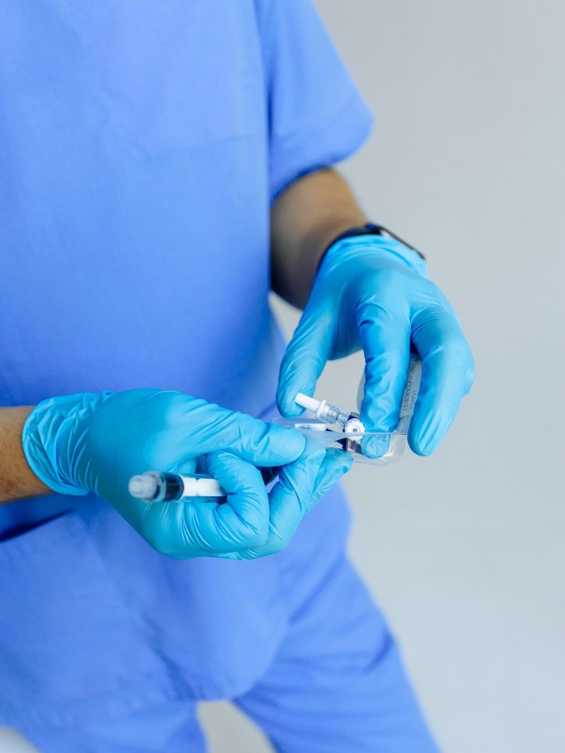 A male nurse wearing surgical gloves opens the packaging of a small piece of medical equipment