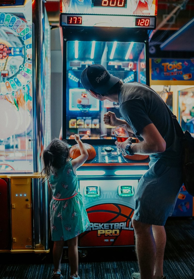 A little girl plays an arcade game with her dad