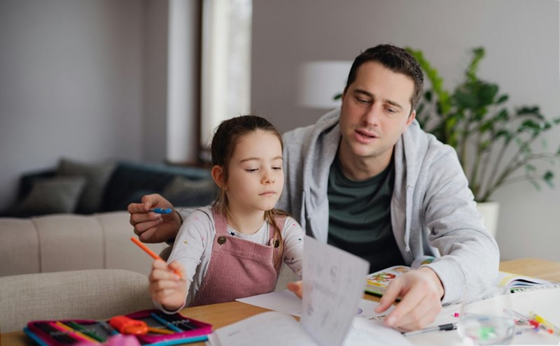 Father helping small daughter with homework indoors
