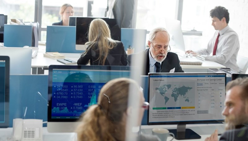 Busy newsroom doing research and typing on their desktop computers, dressed professionally.