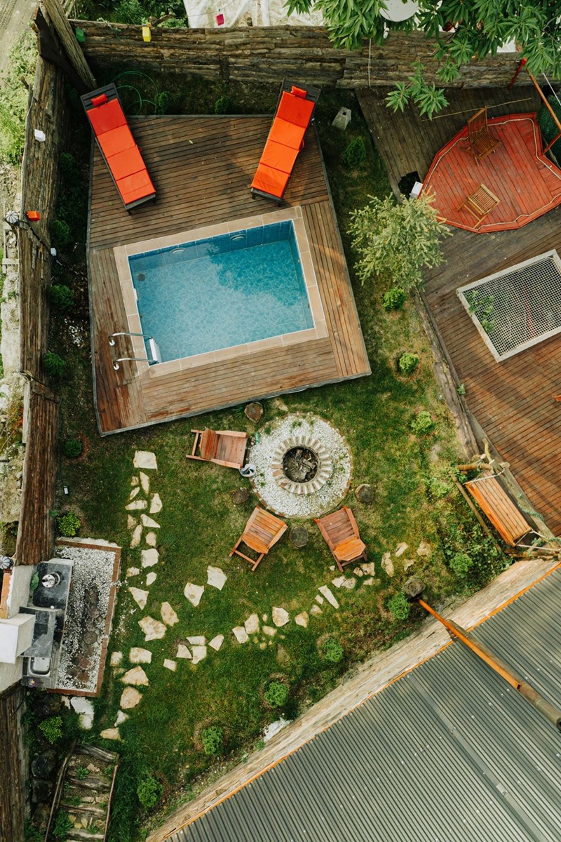 Top-down view of a backyard with a small pool, lounge chairs, wooden deck, and a fire pit surrounded by seating.