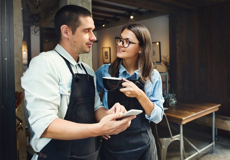 A manager holding his phone and an employee holding a cup of coffee outside of a cafe