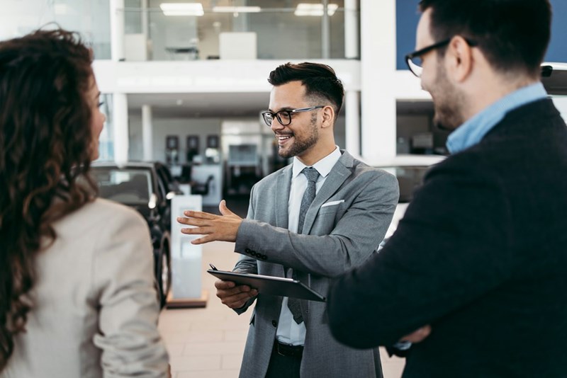 Woman shops for a car with 2 salesmen while her friend takes care of her child.