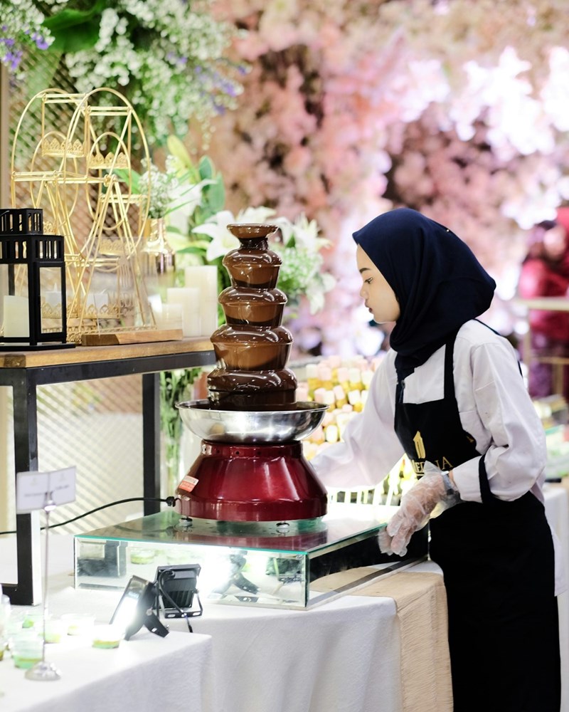 Elegant chocolate fountain on a wedding dessert table, with melted chocolate flowing gracefully from top to bottom.